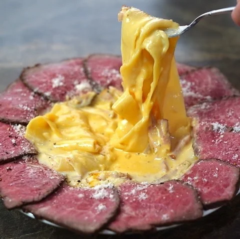 フォークで持ち上げられたクリームソースのパスタが、薄切りのローストビーフに囲まれて盛り付けられた料理。粉チーズがかけられ、食欲をそそる一皿です。