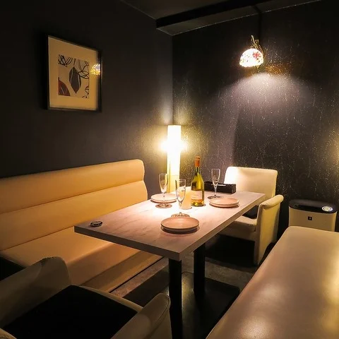 落ち着いた照明が印象的な、モダンな内装のレストランまたはバーの個室です。テーブルにはワインボトルとグラスが用意されており、デートや会食に最適な雰囲気を演出しています。