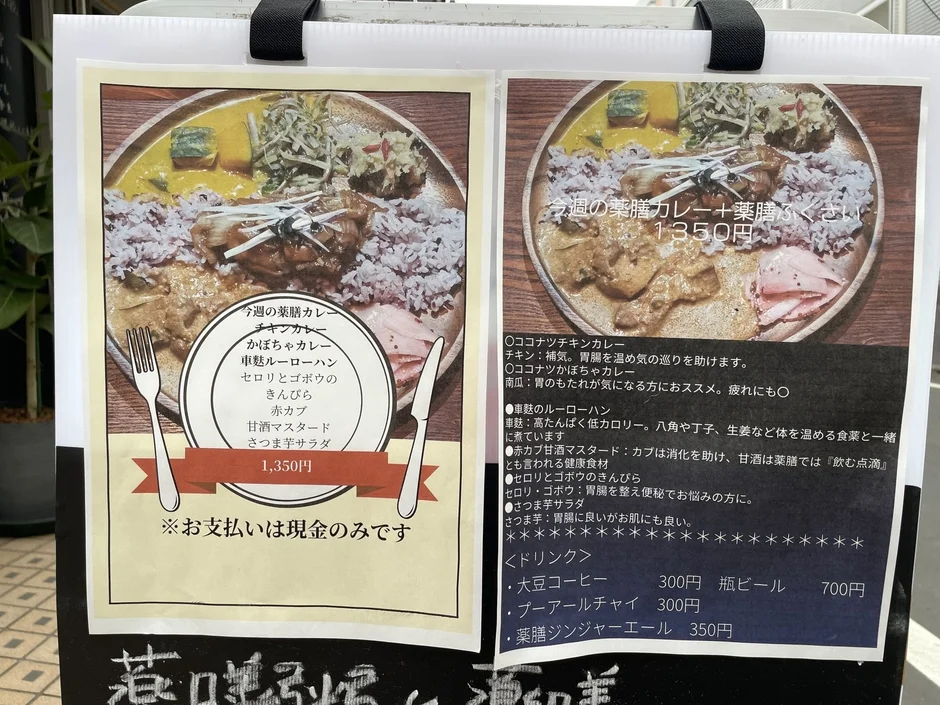 薬膳料理を提供する店のメニューボードです。今週の薬膳カレープレートは1,350円で、チキンカレー、かぼちゃカレー、車麩ルーローハン、副菜などが含まれます。各料理の効能も詳しく説明されており、ドリンクメニューもあります。支払いは現金のみです。