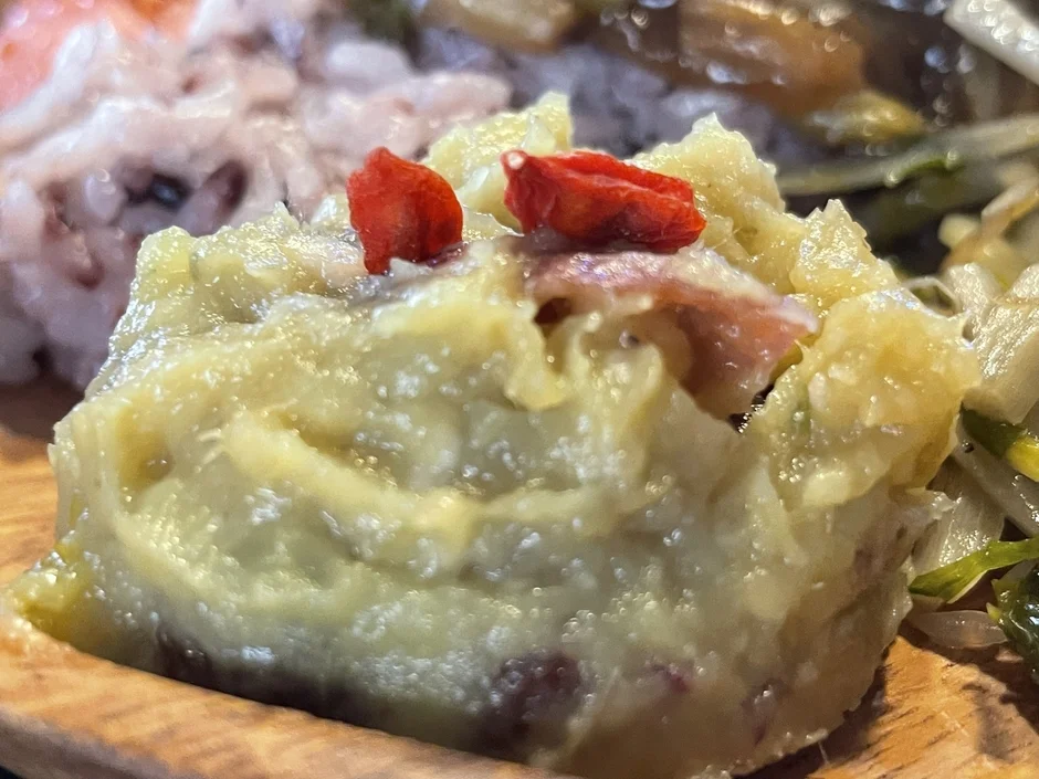 木製の皿に盛られたマッシュ状の料理のクローズアップ画像です。おそらくポテトサラダで、中に肉片が見え、上には赤いクコの実が二つ飾られています。美味しそうな一品です。