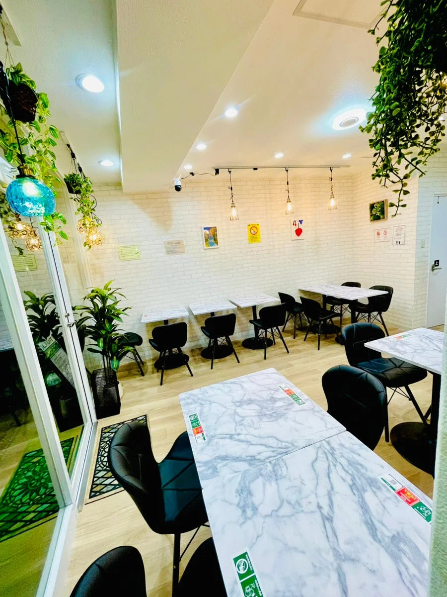 Qder self cafe 針中野駅前店の店内の様子。白いレンガの壁に大理石調のテーブルと黒い椅子が並び、多くの観葉植物が飾られている。