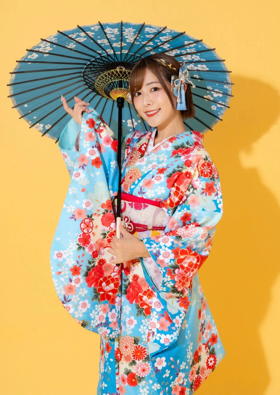 鮮やかな花柄の青い振袖を着た女性が、青い和傘を手に持ち、明るい笑顔