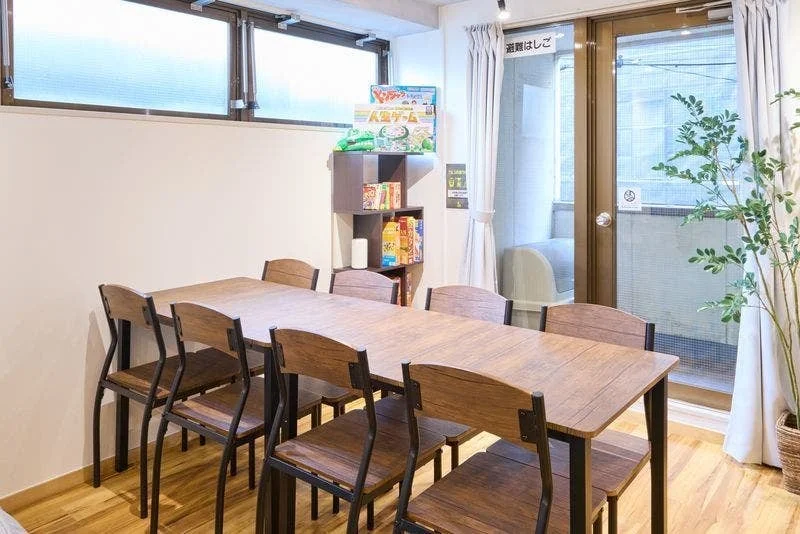 木製の大きなテーブルと椅子が並ぶ、明るく開放的な共有スペース
