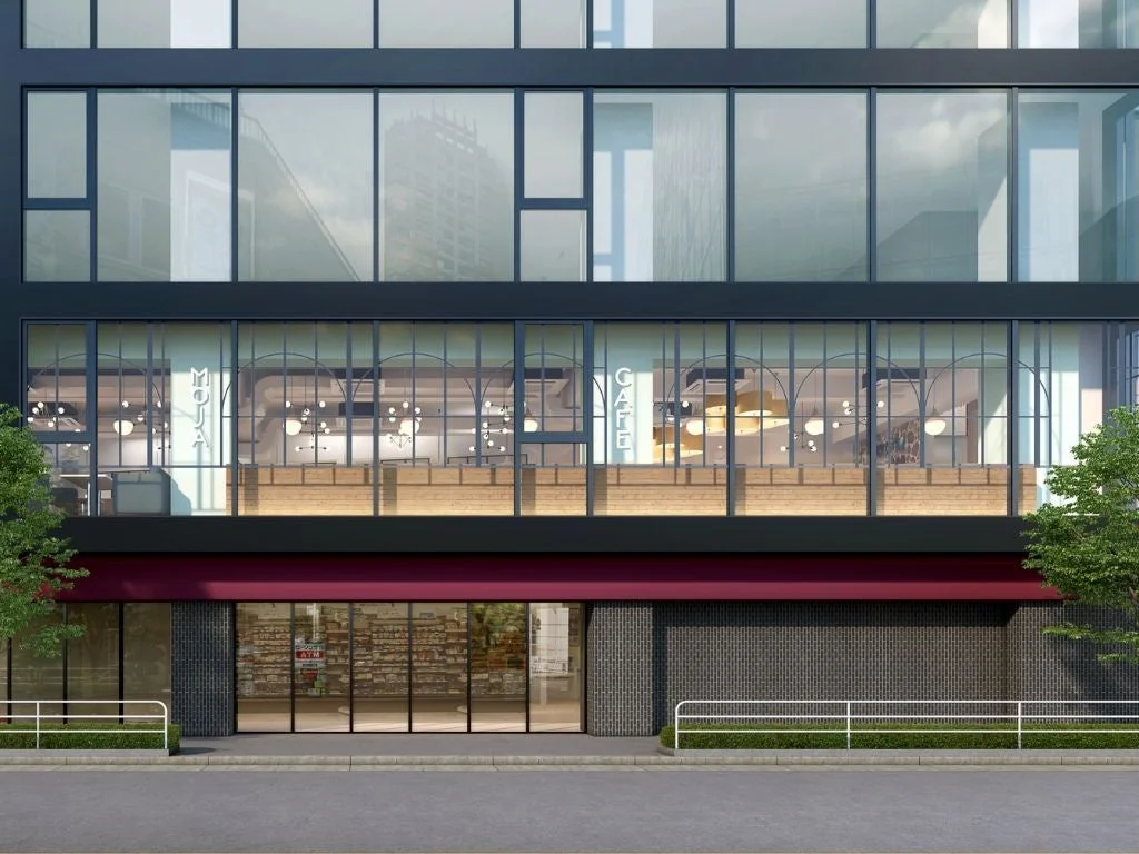 モダンな建物の正面を捉えた画像。2階には「MOJA CAFE」の文字が見えるカフェがあり、1階には「営業中 ATM」の表示がある店舗が入る商業施設。ガラス張りの洗練された都市景観です。