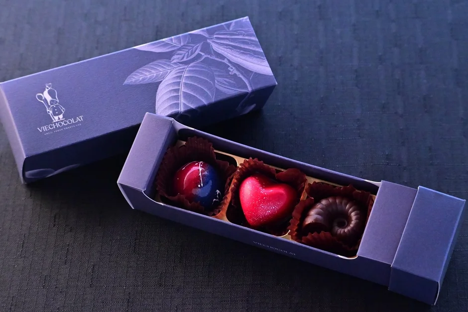 紫色の箱に、ハート型、球状、渦巻き型の3つの美しいチョコレート