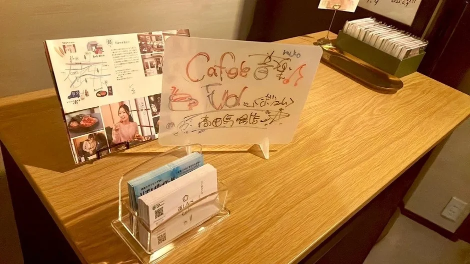 カフェの木製テーブルに、手書きの案内板、メニューパンフレット、名刺立て
