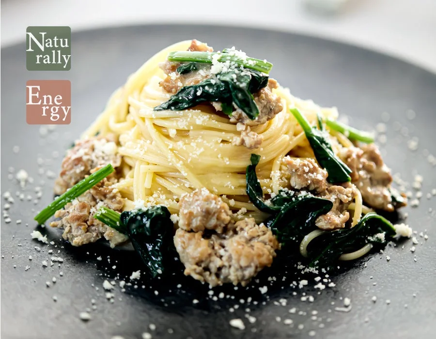 黒い皿に盛られた、ほうれん草とひき肉（またはソーセージ）のパスタ料理