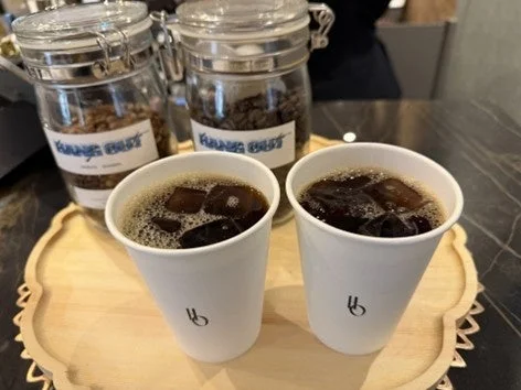 木製トレイに置かれた2つの白い紙コップに入ったアイスコーヒー