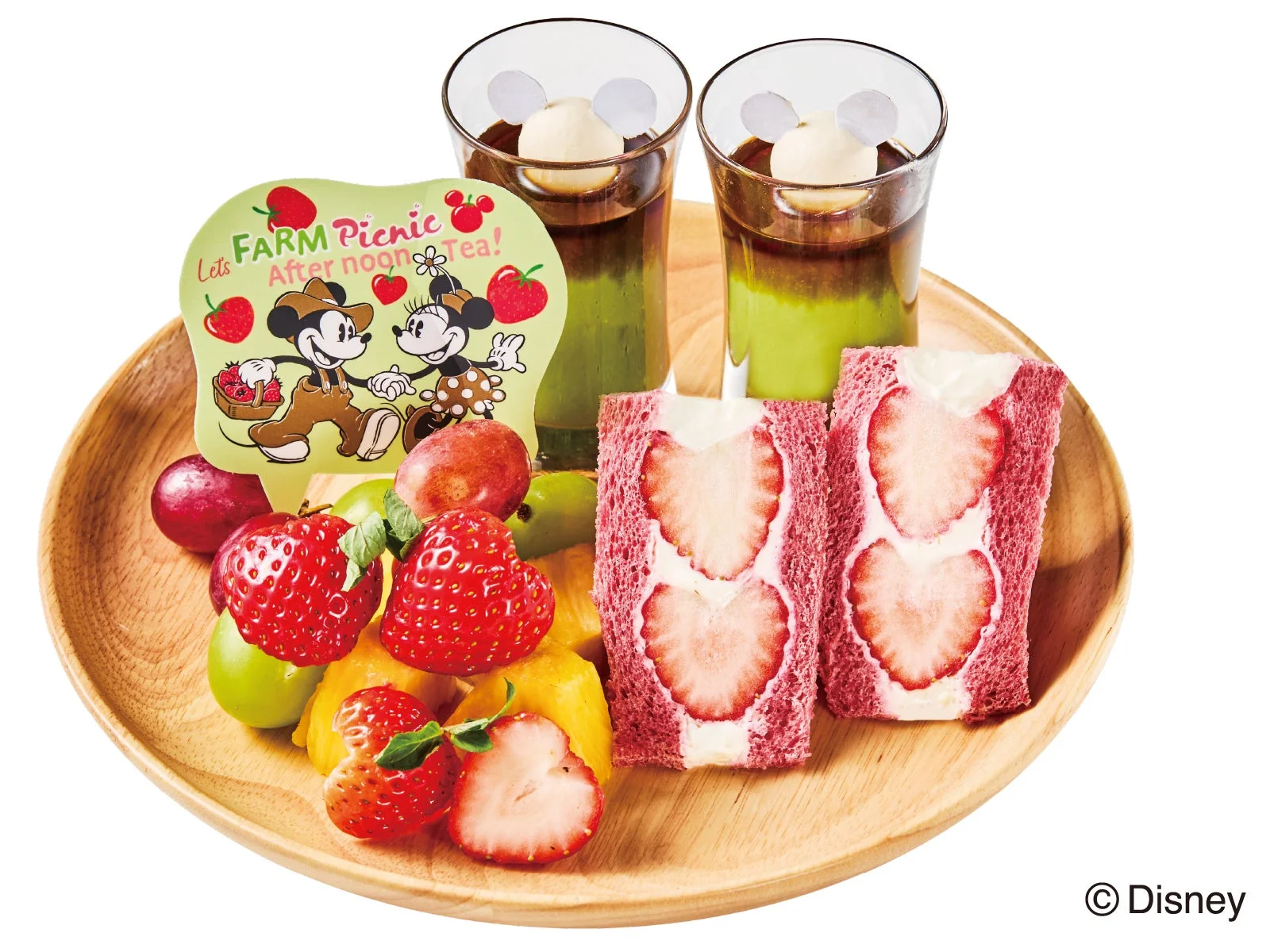 ミッキーとミニーがテーマの可愛らしいアフタヌーンティーセット。いちごのフルーツサンド、フレッシュなフルーツ、ミッキーの耳が飾られた抹茶ドリンクが木製プレートに並び、農園ピクニックをイメージしたデザートです。