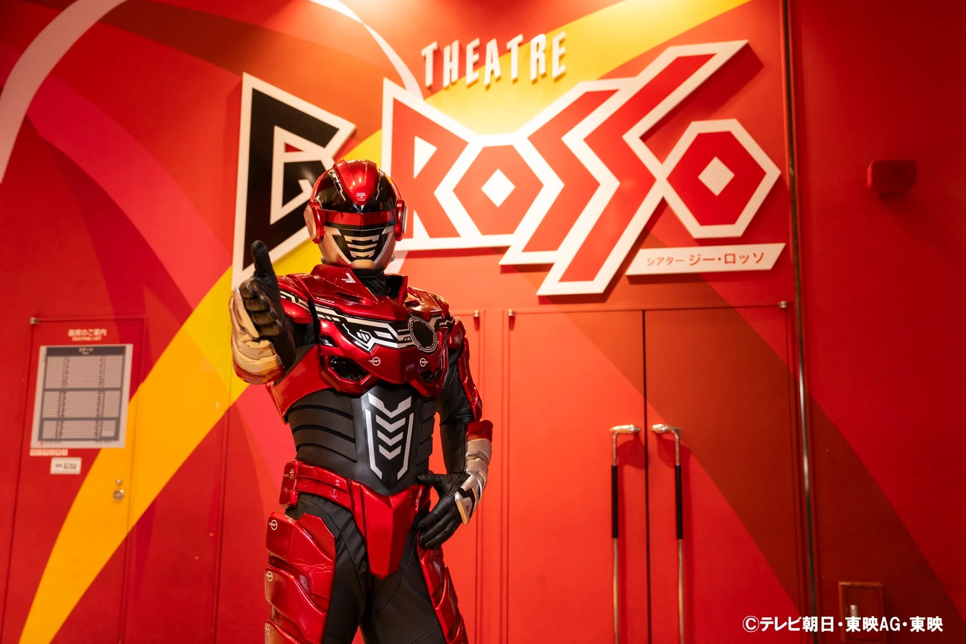 シアターGロッソの赤い壁の前でポーズをとるヒーロー