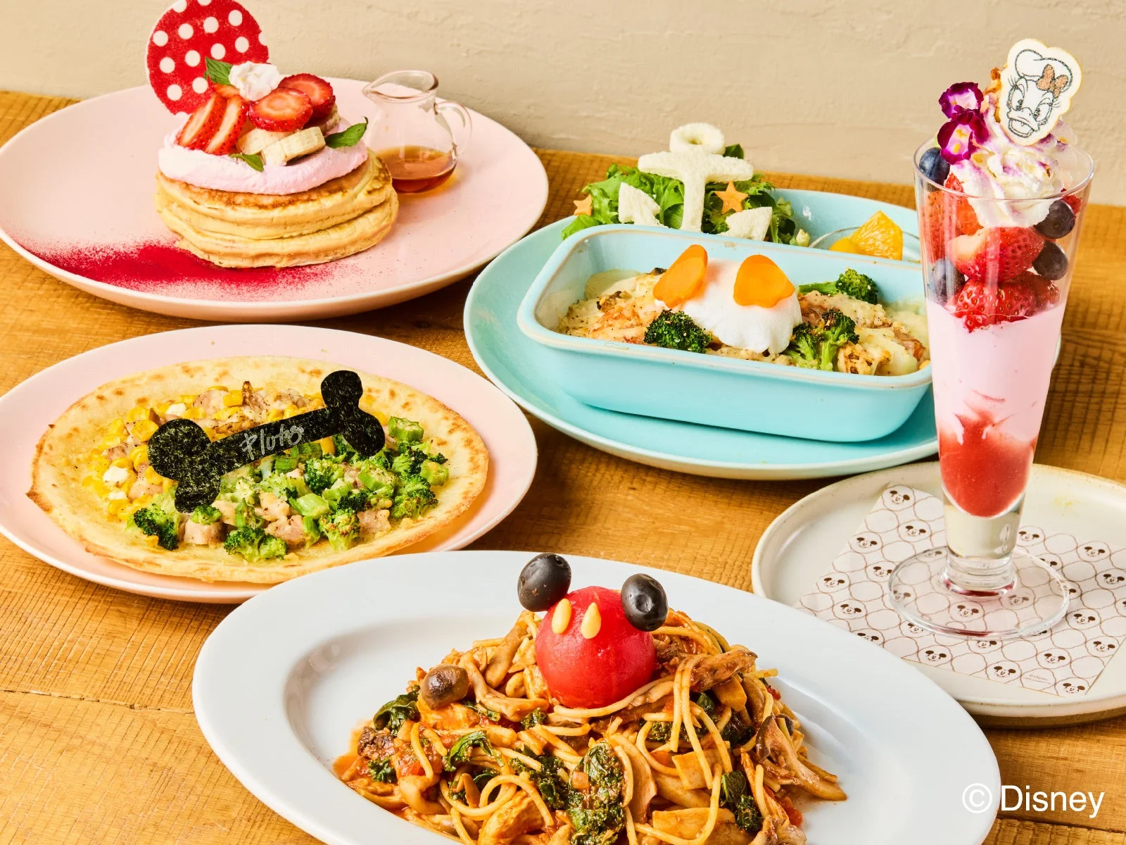 ディズニーキャラクターをモチーフにした彩り豊かな料理とデザートが並ぶテーブルの様子。ミッキー、ミニー、ドナルド、プルート、デイジーをイメージしたパンケーキ、パスタ、グラタン、ガレット、パフェが食欲をそそる。