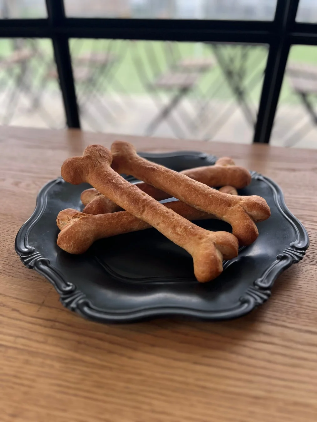 黒い装飾的な皿に盛られた骨の形をしたパンやクッキーが木製のテーブルに置かれています。