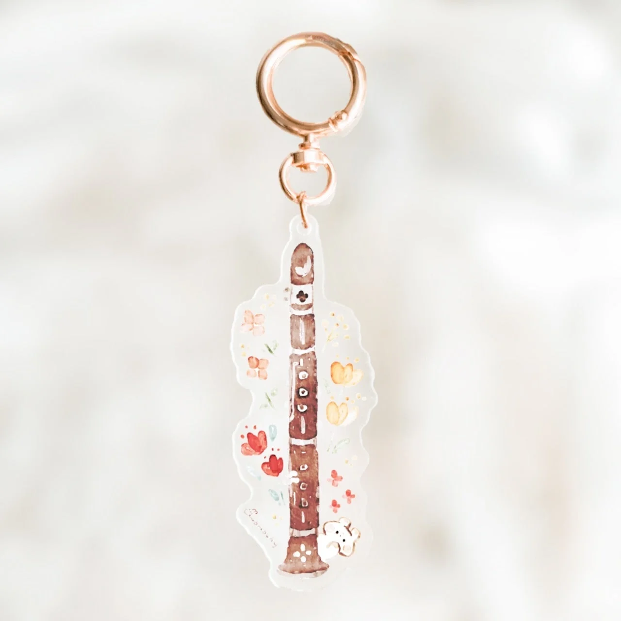 ローズゴールドの金具が付いたクラリネット型のキーホルダー。水彩画風のクラリネットには花や蝶、小さな白い動物が描かれている