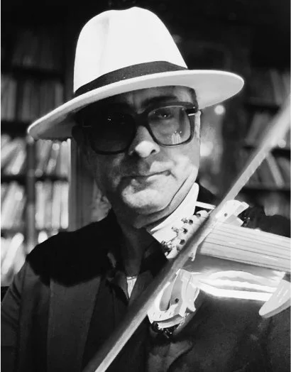 白いフェドラ帽と眼鏡をかけた男性がバイオリンを演奏しているモノクロ写真。