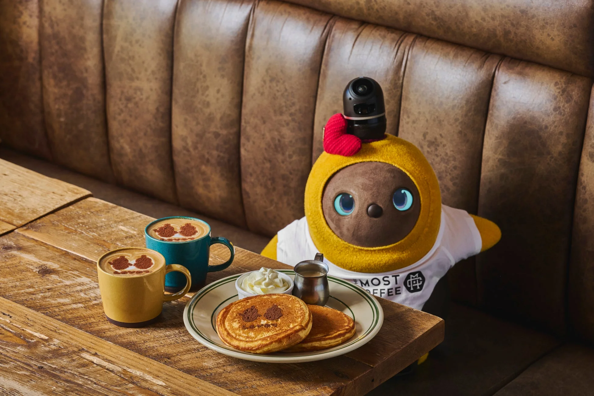 カフェのブース席に座るLOVOTがコーヒーとパンケーキを楽しんでいる