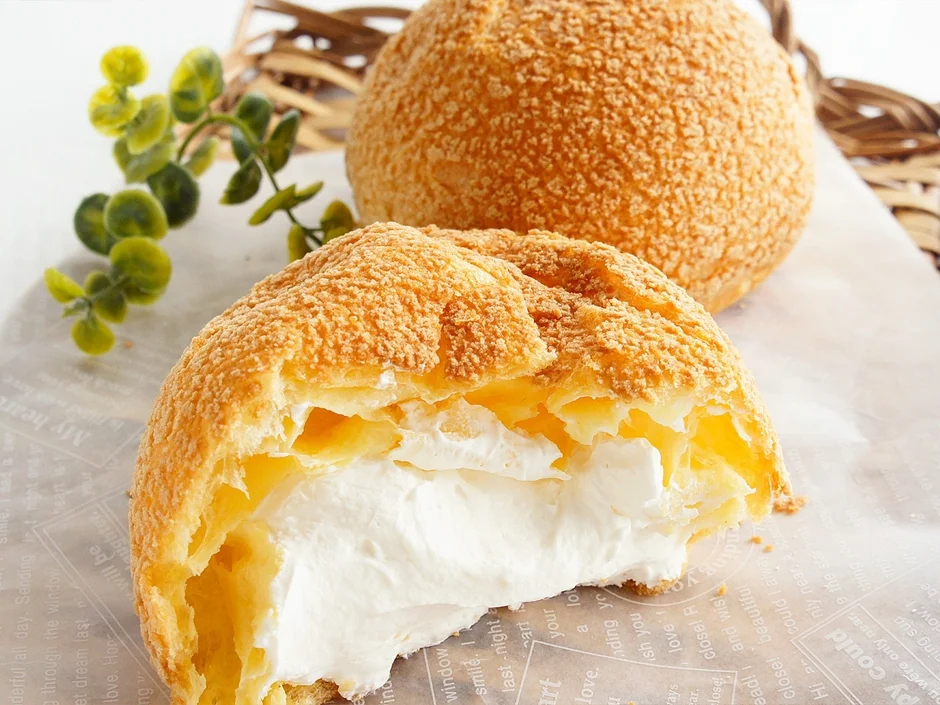 サクサクとした皮のシュークリームが2つ写っており、手前のものは半分にカットされ、たっぷりの白いクリームが詰まっている様子