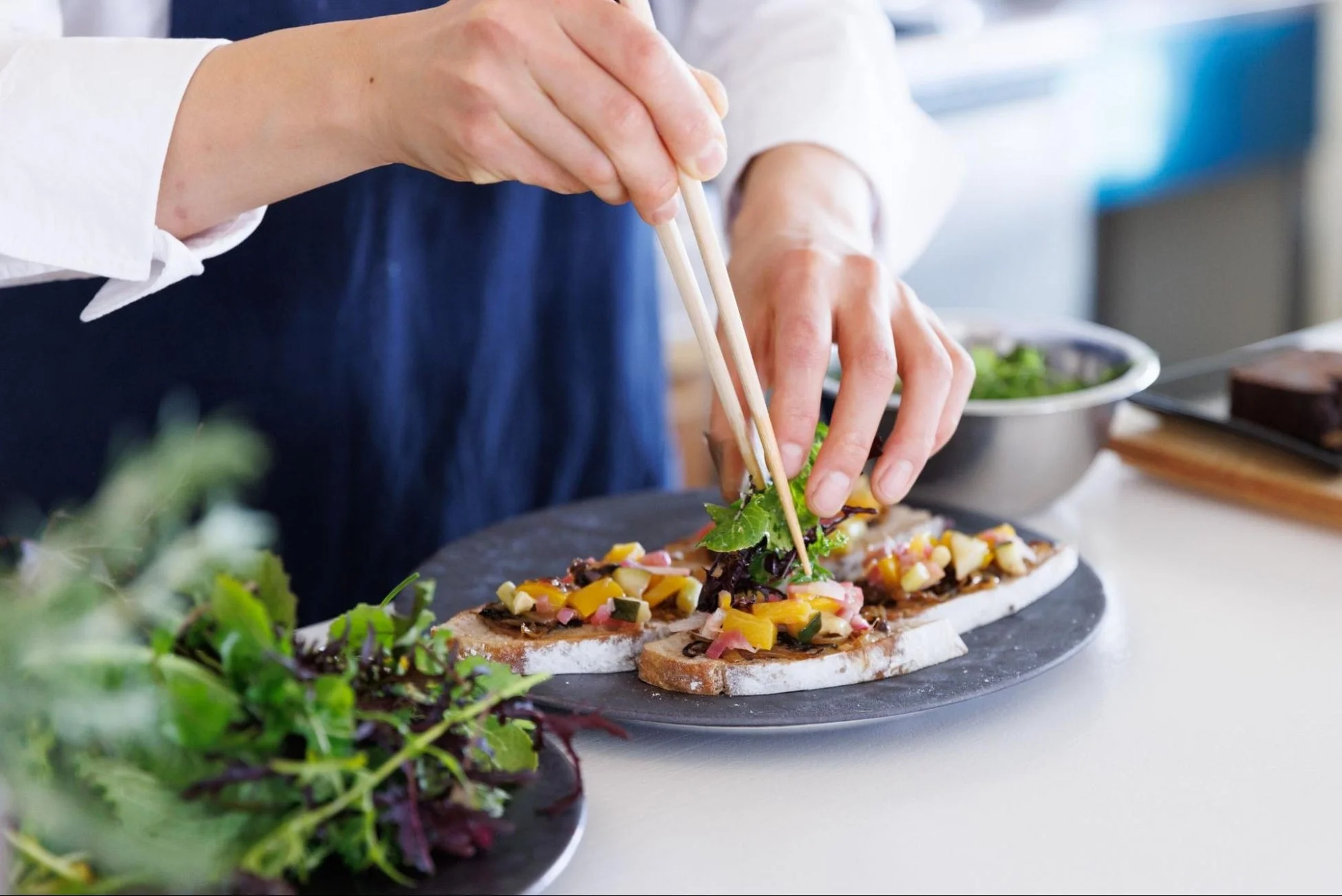 料理人がトーストに彩り豊かな野菜を盛り付けている様子