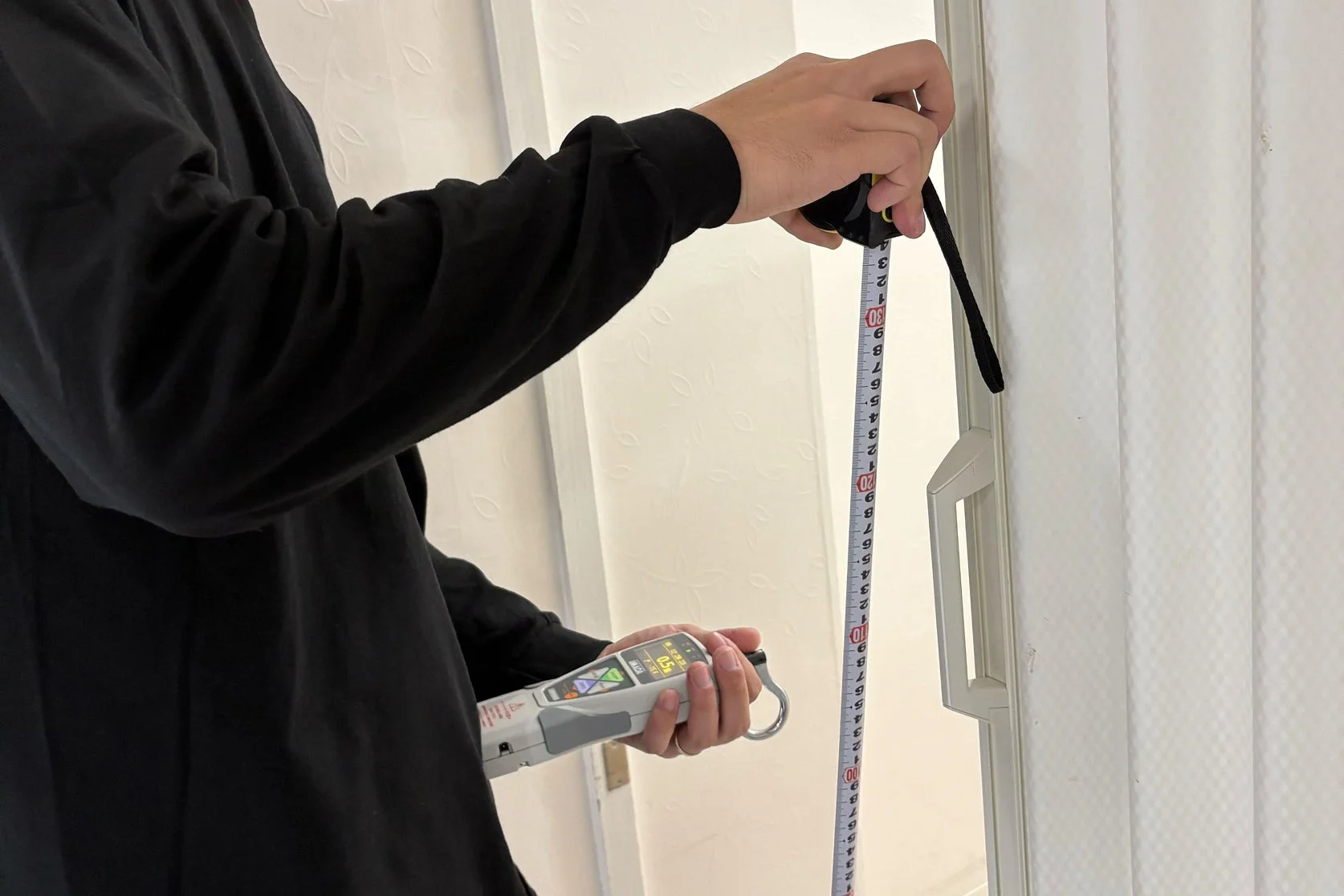 屋内で作業者がメジャーとデジタルフォースゲージを使い測定を行っている。フォースゲージの表示は「0.50」で、最大値を示している。