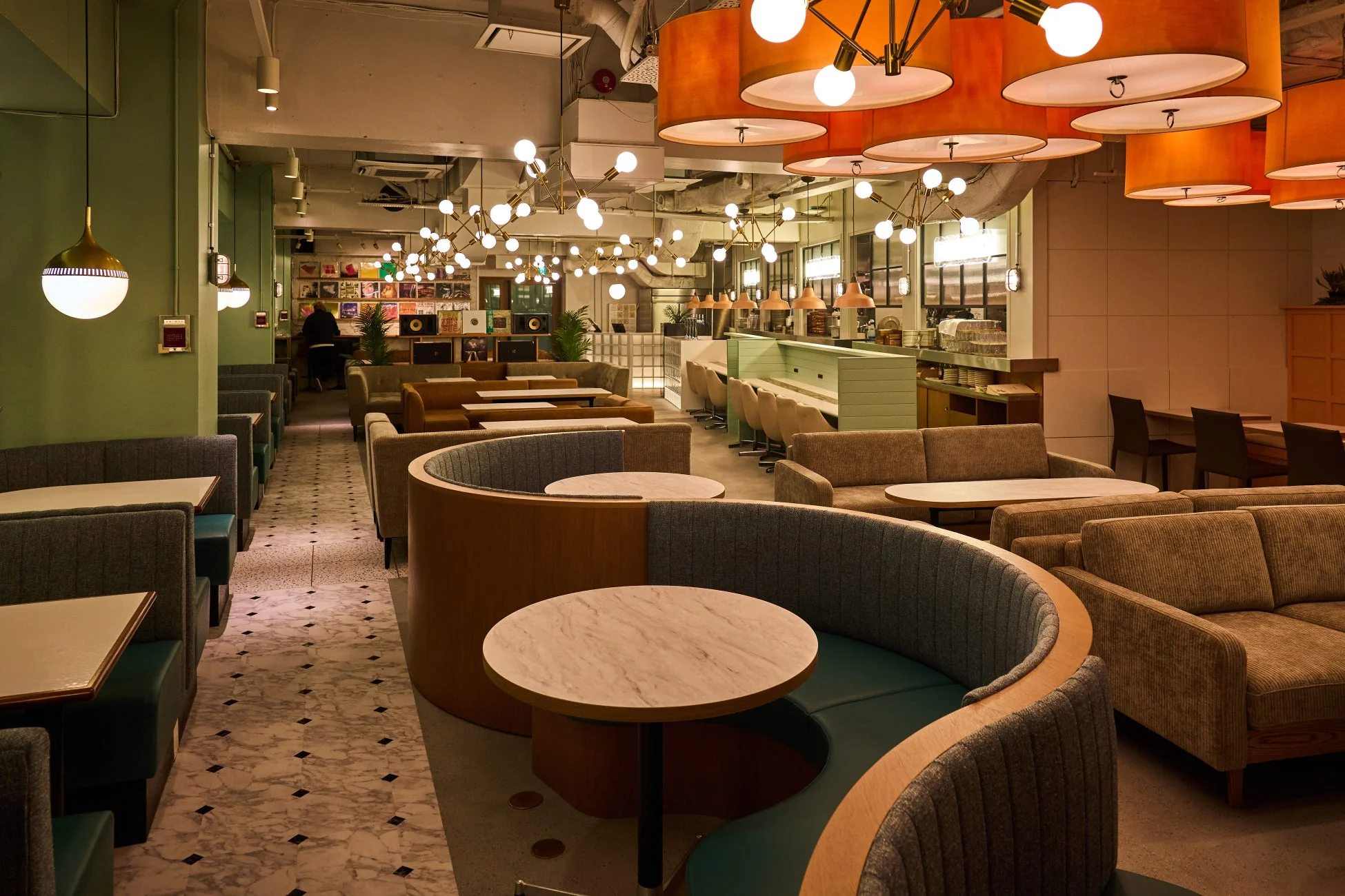 様々なタイプの座席と特徴的な照明器具が配置された、モダンでおしゃれなカフェまたはラウンジの店内風景です。壁にはレコードが飾られ、落ち着いた雰囲気があります。