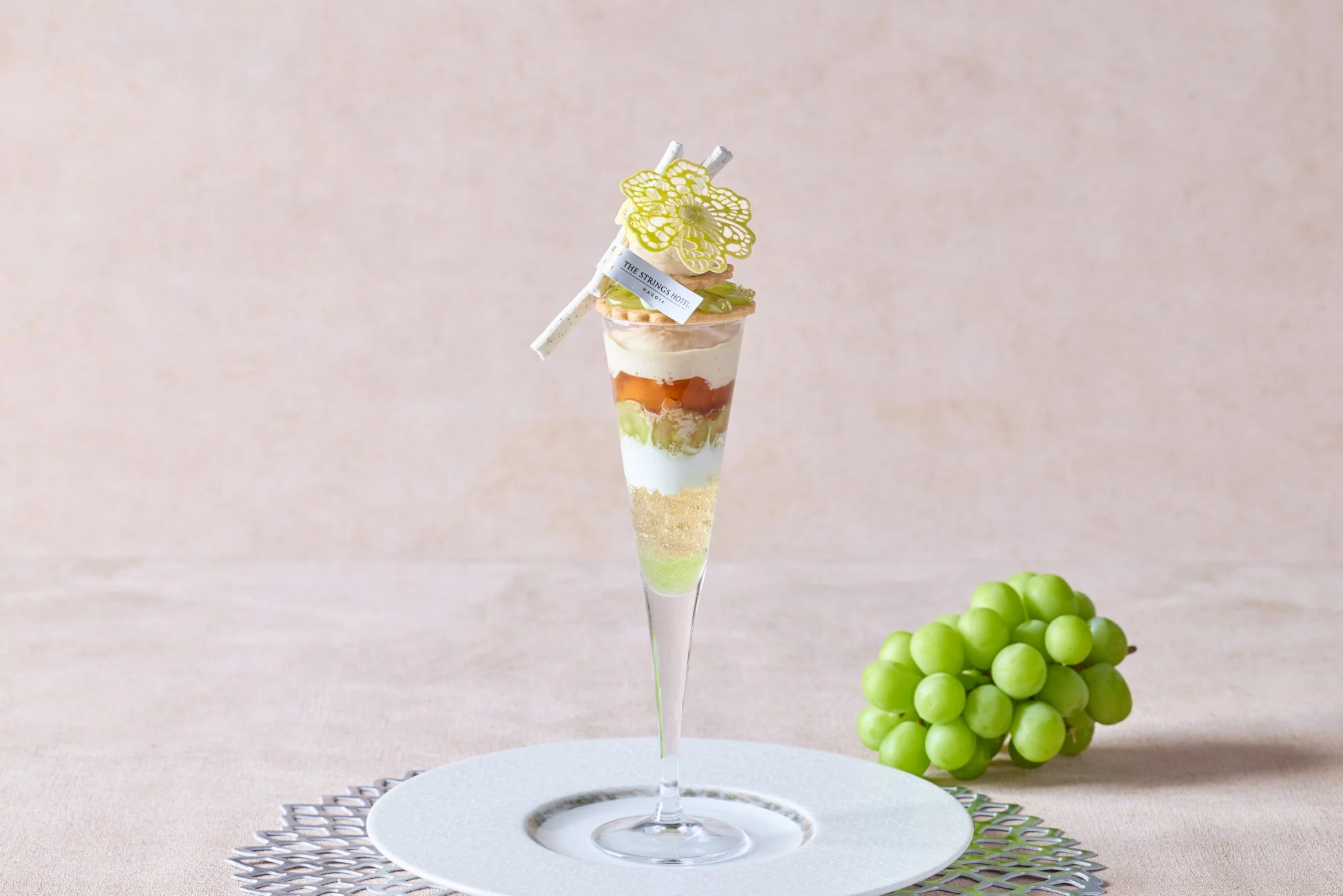 透明なグラスに盛られた美しいパフェと、その横に置かれた新鮮な緑色のぶどうの房