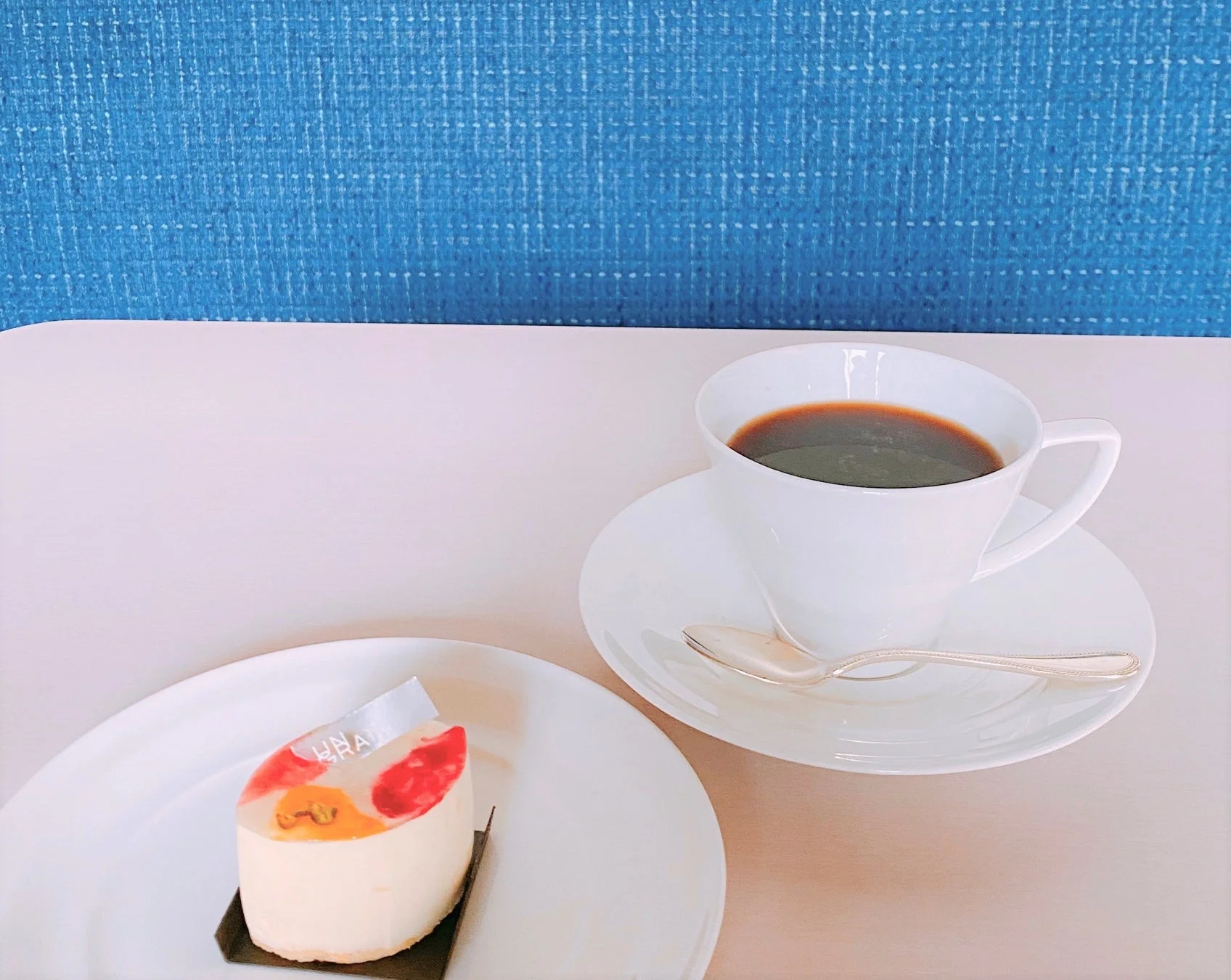 白いテーブルに置かれたコーヒーカップと、フルーツが飾られた白いケーキが写っています。