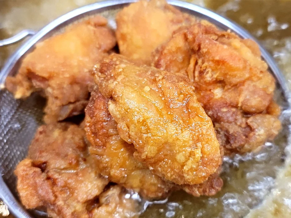 揚げたての唐揚げが金属製の網に入れられ、余分な油を切っている様子