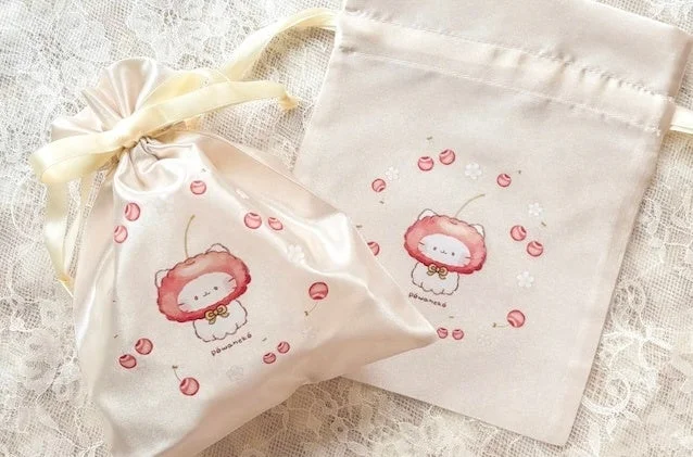 さくらんぼの帽子をかぶった可愛い猫のイラストが描かれたクリーム色の巾着袋