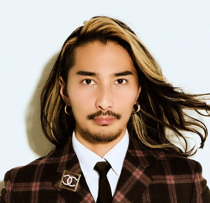 長髪にハイライトが入った髪型と髭が特徴的な男性のポートレート