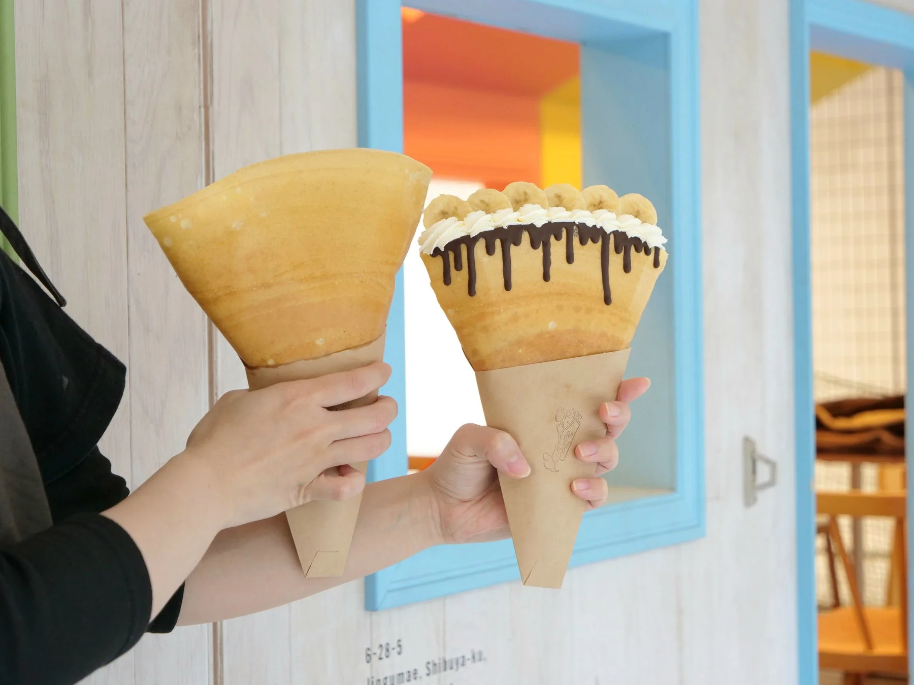 バナナ、ホイップクリーム、チョコレートソースがトッピングされたクレープを持つ手