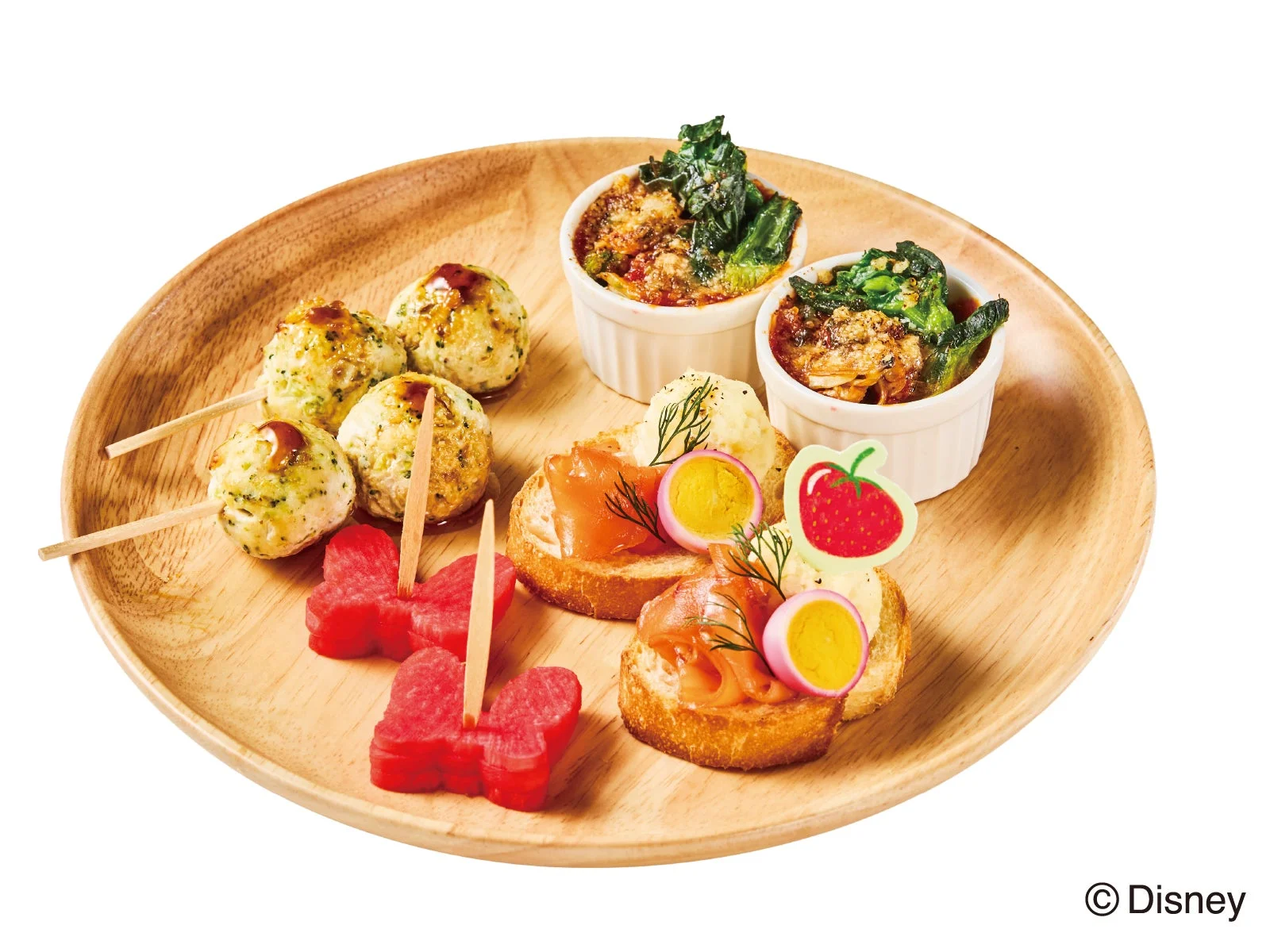 木製のプレートに盛り付けられた、色とりどりのアペタイザーのセットです。ミートボール、サーモンのカナッペ、ミニグラタン、蝶々型のスイカなどが含まれています。