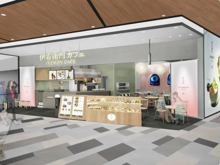 「伊右衛門カフェ」のモダンで明るい内装の店舗の様子です。ショーケースにはスイーツが並び、メニューボードやテーブル席も確認できます。人々が行き交う商業施設内にあるようです。