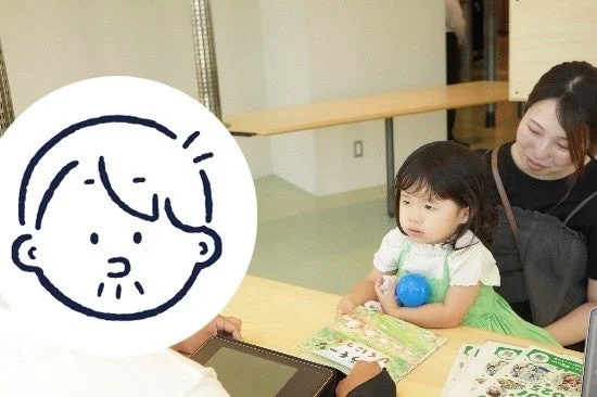 子供と大人がテーブルで本を見ている画像