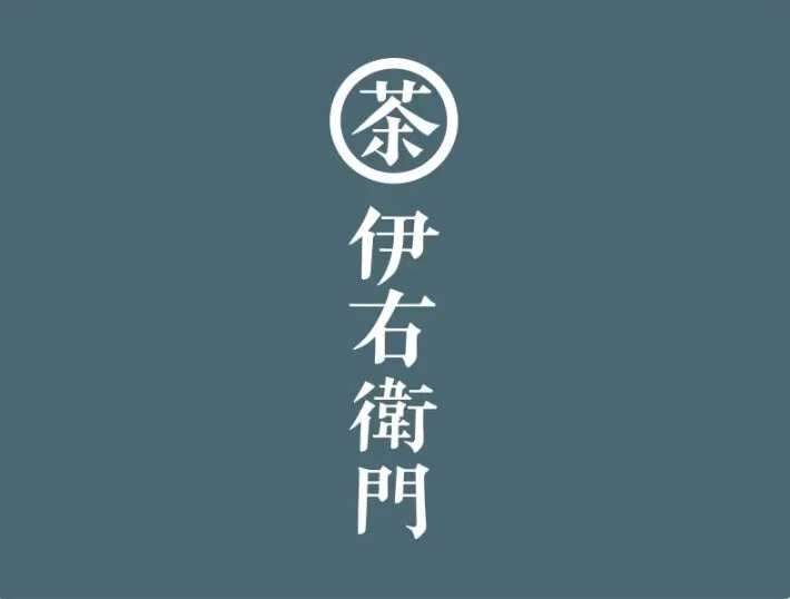 濃い青みがかったグレーの背景に、白抜きで「茶」の文字が丸で囲まれ、その下に縦書きで「伊右衛門」と書かれたロゴマーク。日本の伝統的なお茶のブランドを思わせるデザインです。