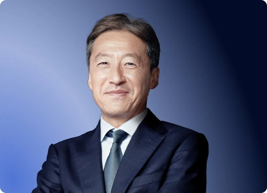 青いグラデーションの背景を背に、ダークスーツとネクタイを着用したアジア系の男性が、穏やかな笑顔を浮かべている上半身のポートレート画像です。