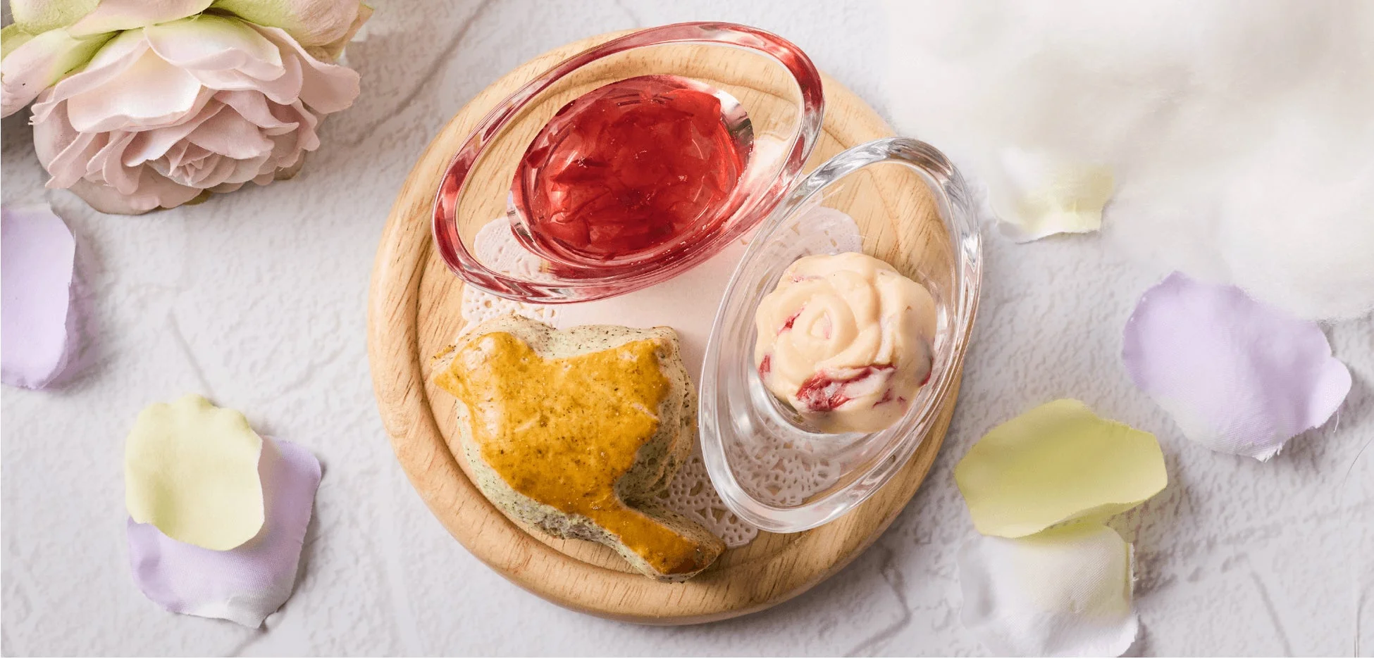 木製プレートに鳥の形をしたスコーン、赤いジャム、バラの形のクリームが並べられています。ピンクのバラとパステルカラーの花びらが散りばめられ、優雅なティータイムを思わせるデザートの盛り合わせです。