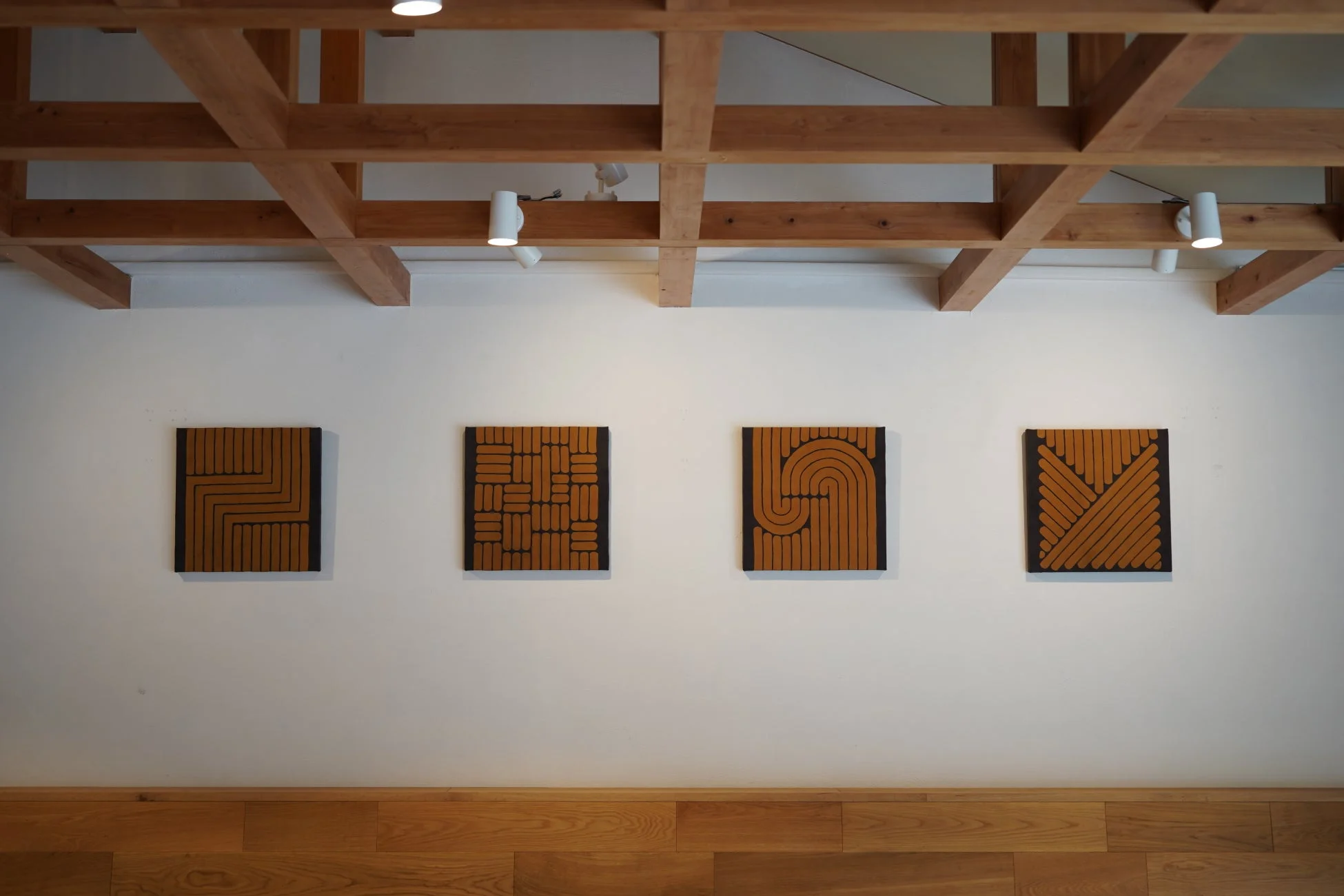 白い壁に4枚の抽象画が飾られ、木製の梁と床が温かみのあるモダンな空間を演出しています。