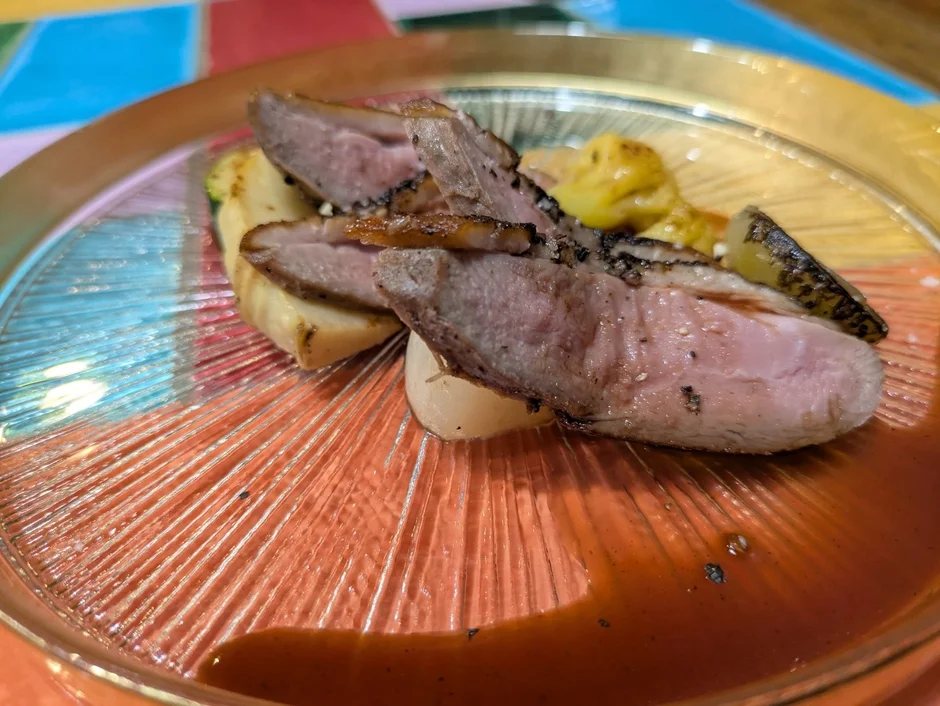 透明なリブ付きの皿に盛り付けられた、皮目が香ばしい鴨肉のロースト。中心がピンク色の肉は絶妙な火加減で、付け合わせの野菜と濃厚なソースが添えられた美しい一皿です。