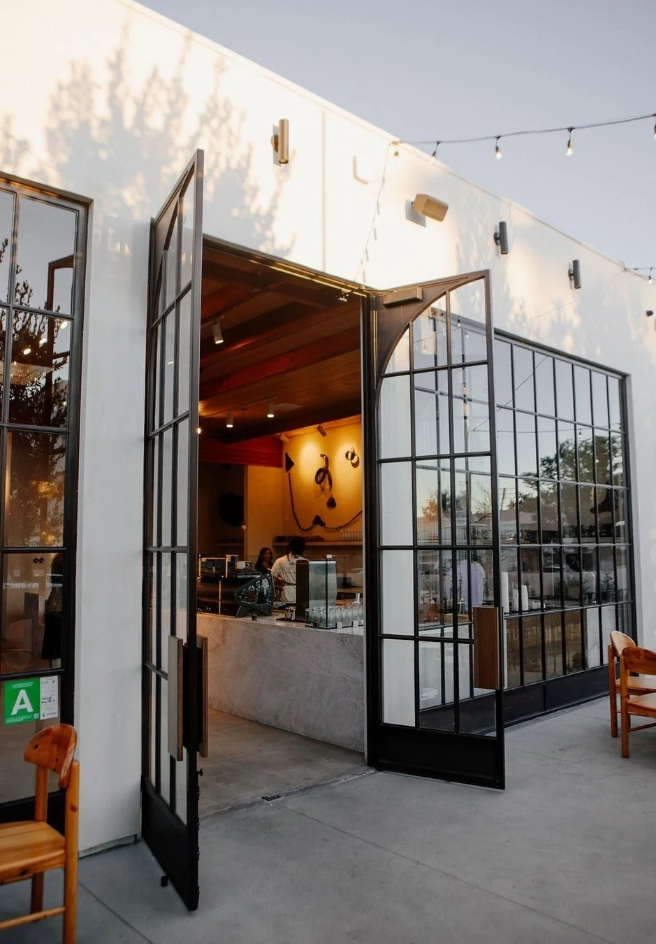 白いモダンな建物に大きなガラス扉が開放されたカフェの外観