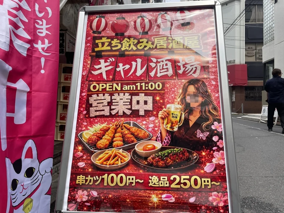 「立ち飲み居酒屋 ギャル酒場」の店頭看板が写っています。串カツや逸品料理、ビールを持つ女性のイラストが描かれており、午前11時から営業中であることが示された賑やかな広告です。