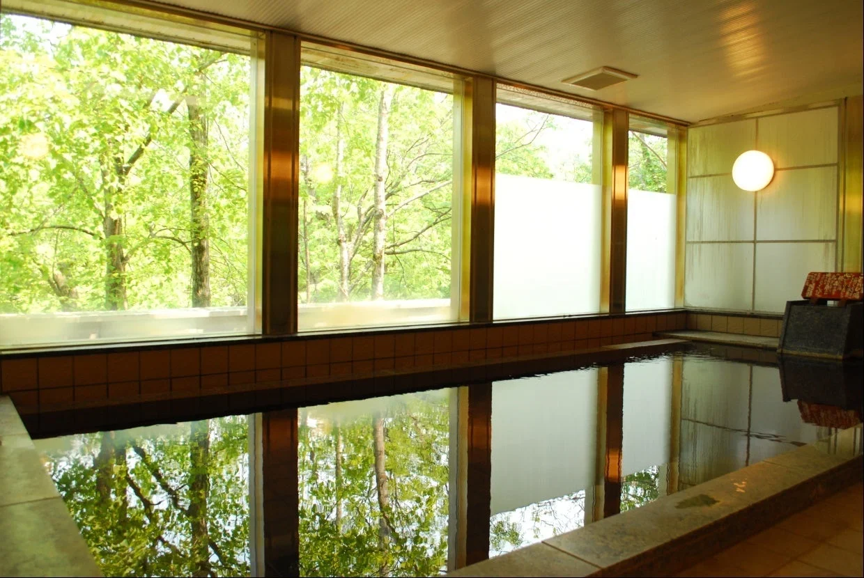 大きな窓から豊かな緑を望む、開放感のある内風呂の風景です。
