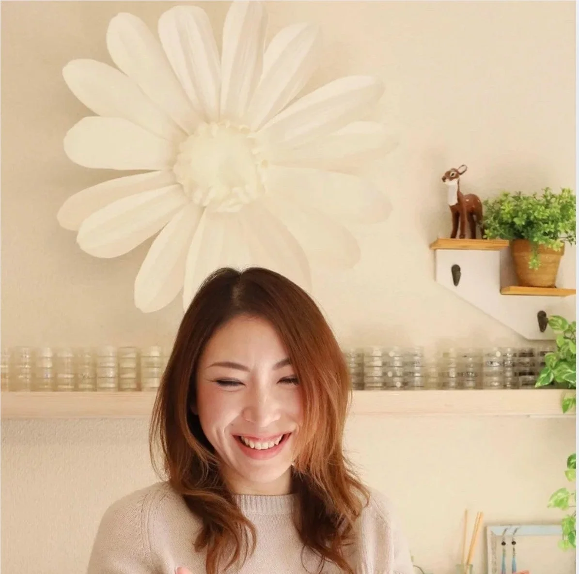 明るい室内で、大きな白い花の壁飾りを背景に、楽しそうに笑っている女性のポートレート