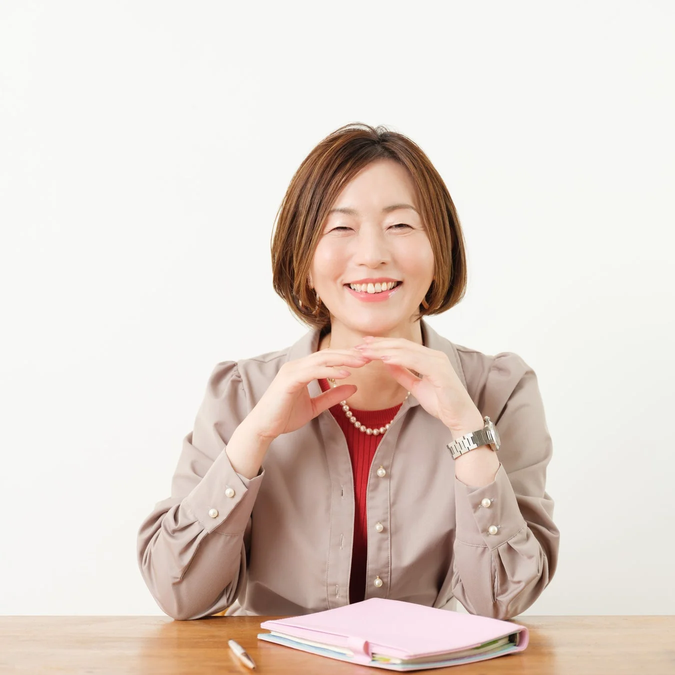デスクに座り、両手を組んで笑顔を見せる日本人女性