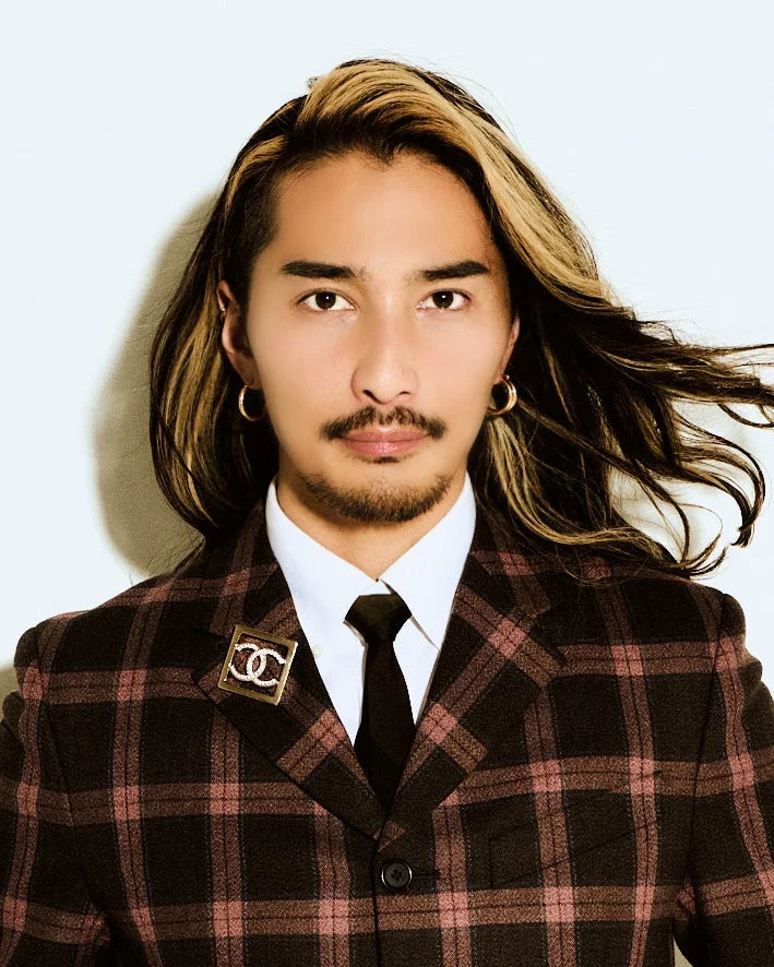 長髪でハイライトの入った髪型と髭が特徴的な男性のポートレート