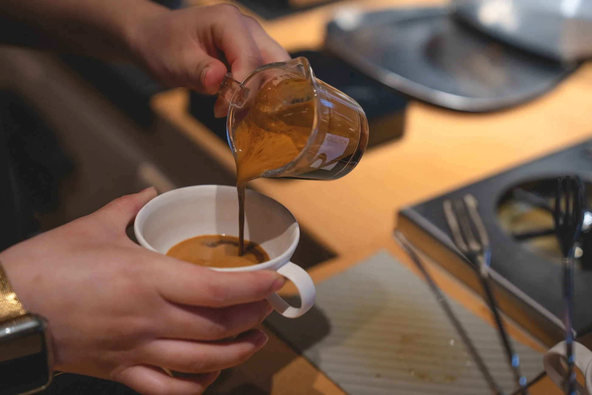 バリスタが計量カップに入ったエスプレッソを白いカップに注いでいる瞬間
