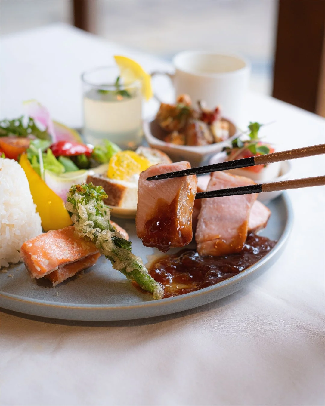 箸で肉料理をつまんでいる様子を捉えた、様々な料理が盛り付けられたプレートの写真