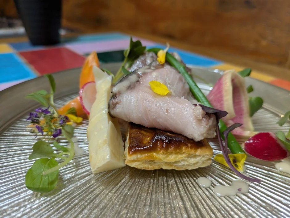 美しく盛り付けられた魚料理のアップショットです。パイ生地の上に魚が乗せられ、ラディッシュやハーブ、花々で彩られています。洗練されたレストランの一皿を思わせる、見た目にも楽しい一品です。
