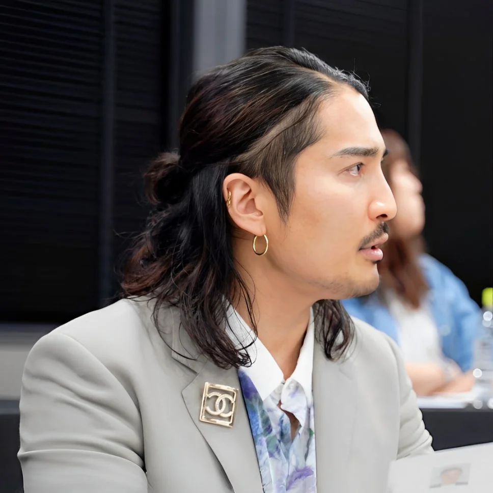 男性がライトグレーのブレザーを着て、シャネルのブローチを付けている