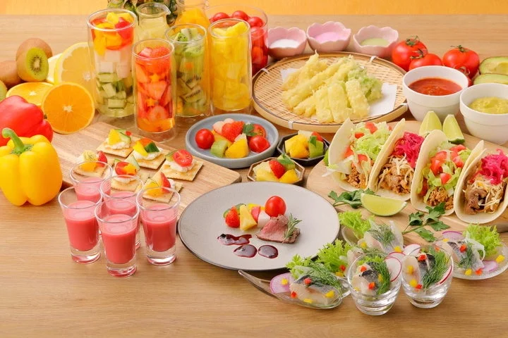 色とりどりの料理が並んだビュッフェスタイルの食卓。フルーツカクテル、タコス、天ぷら、肉料理、魚のマリネなど、様々なジャンルのヘルシーで華やかな料理が豊富に用意されており、パーティーや特別な食事のシーンにぴったりです。