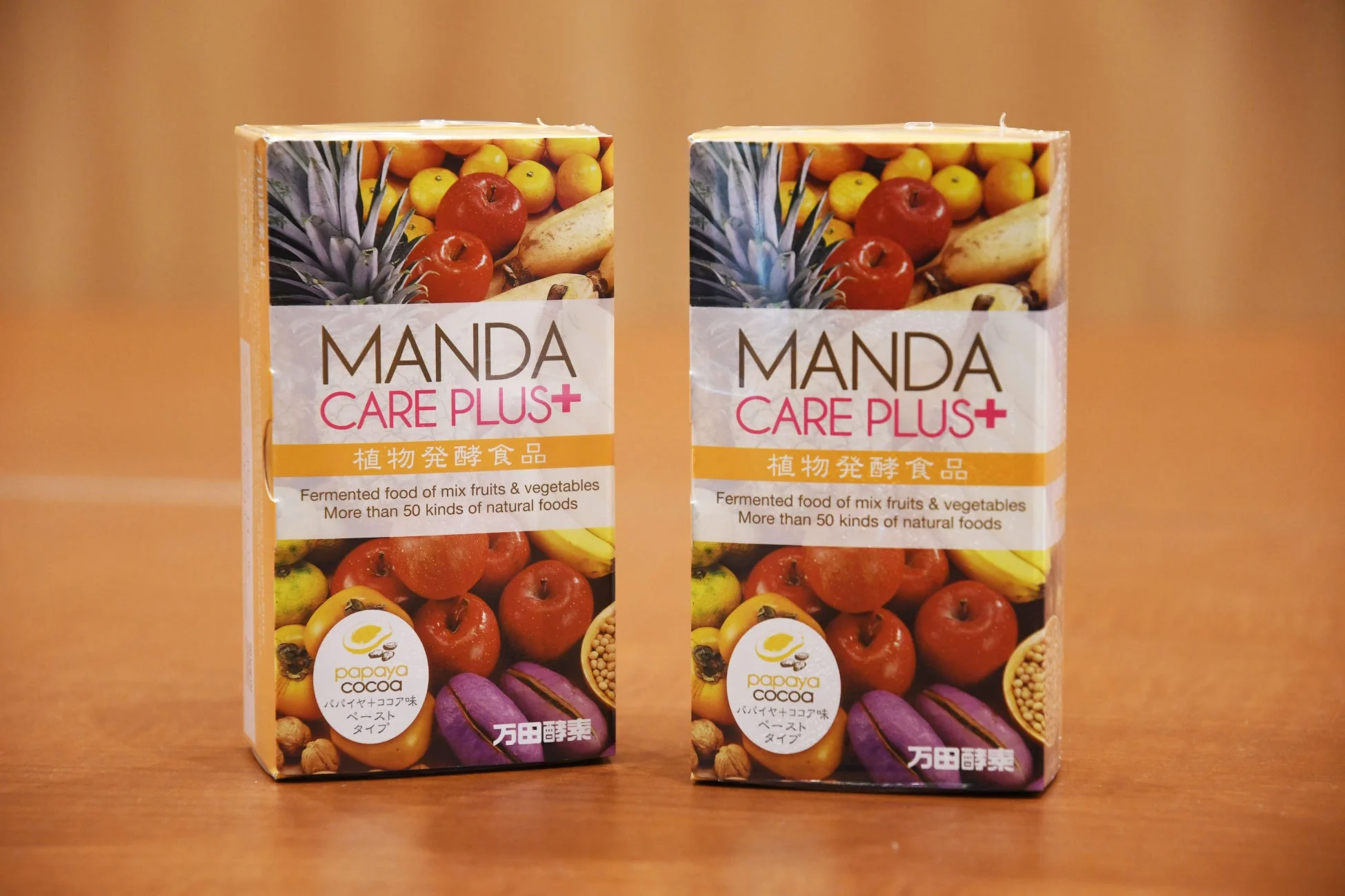 MANDA CARE PLUS+の植物発酵食品の箱が2つ並べられた画像です。パイナップル、リンゴ、バナナなどの果物が描かれており、パパイヤ+ココア味のペーストタイプであることがわかります。
