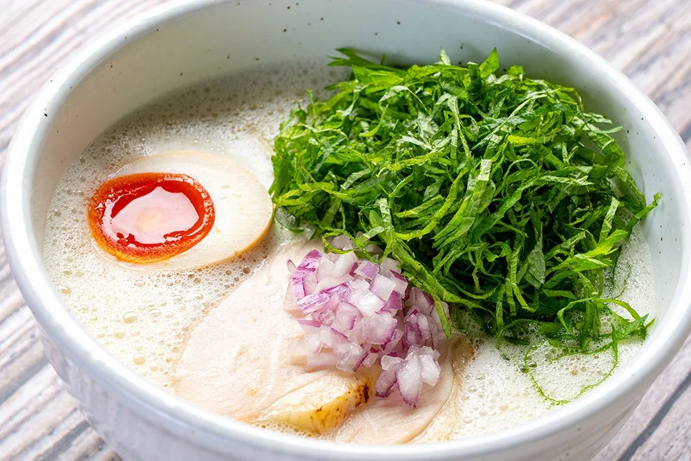 泡立つ白いスープのラーメン、半熟卵、鶏チャーシュー、刻み紫玉ねぎ、大葉
